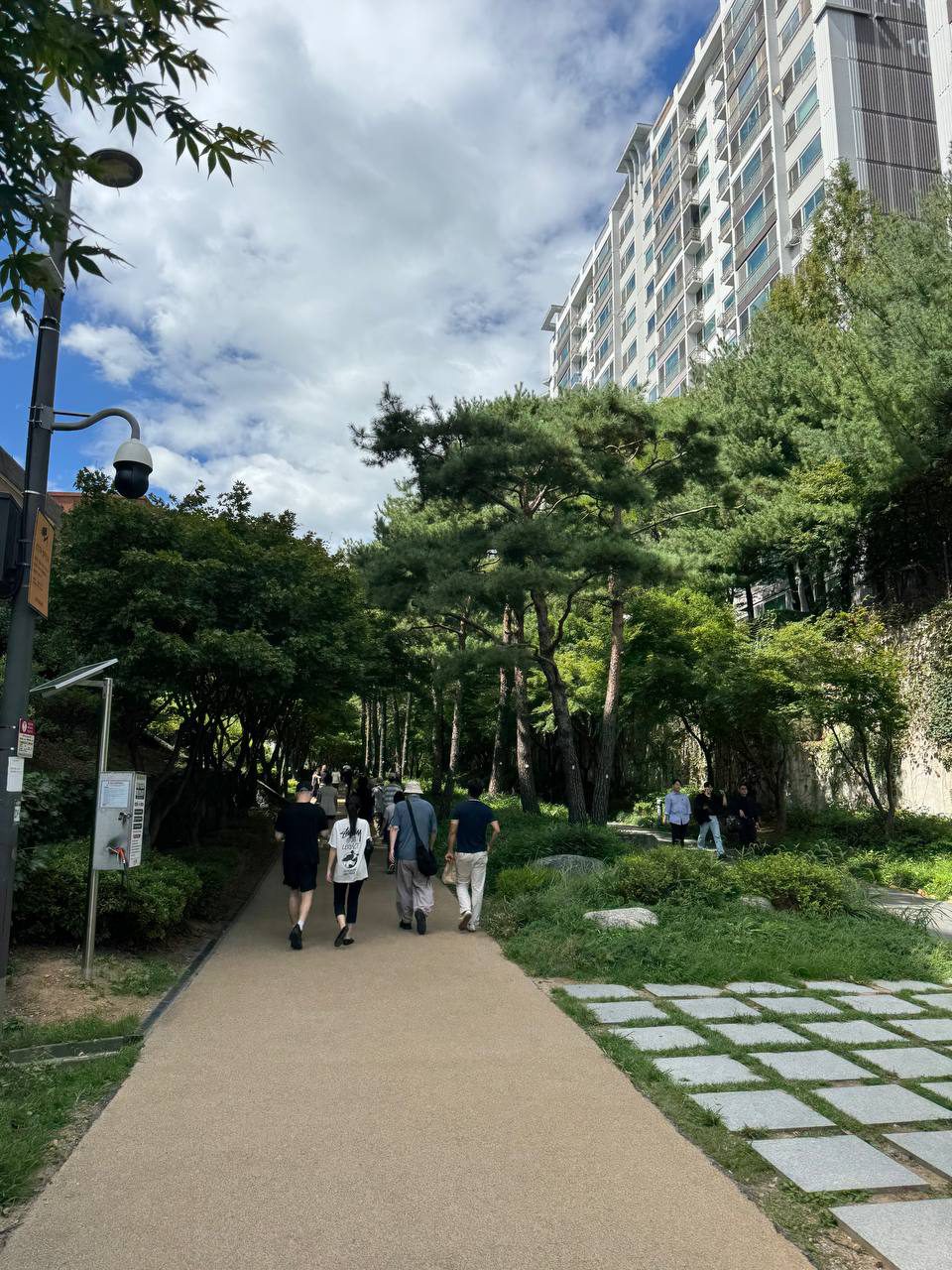 완만한 오르막 산책로를 사람들이 걸어 올라가고 오른쪽 옹벽 위로 아파트가 서 있는 풍경