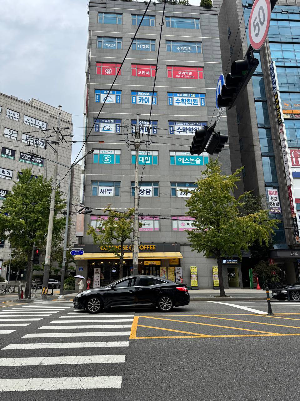 회색 건물 외벽 창문마다 수학학원, 국어학원, 카이, 에스논술 간판이 층층이 붙어 있고 1층에 컴포즈커피가 있는 대흥역 사거리 건물